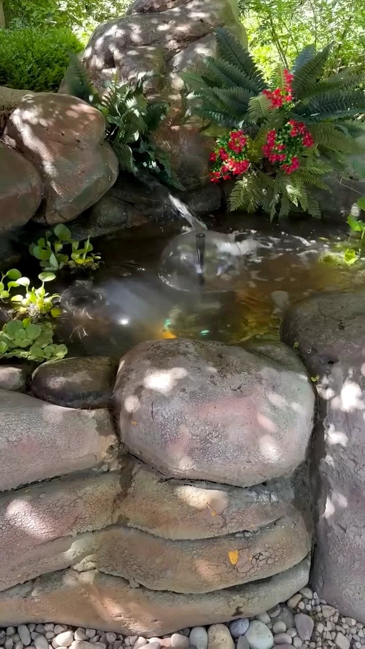 Real rock-lined backyard pond with water flowing between boulders and garden plants